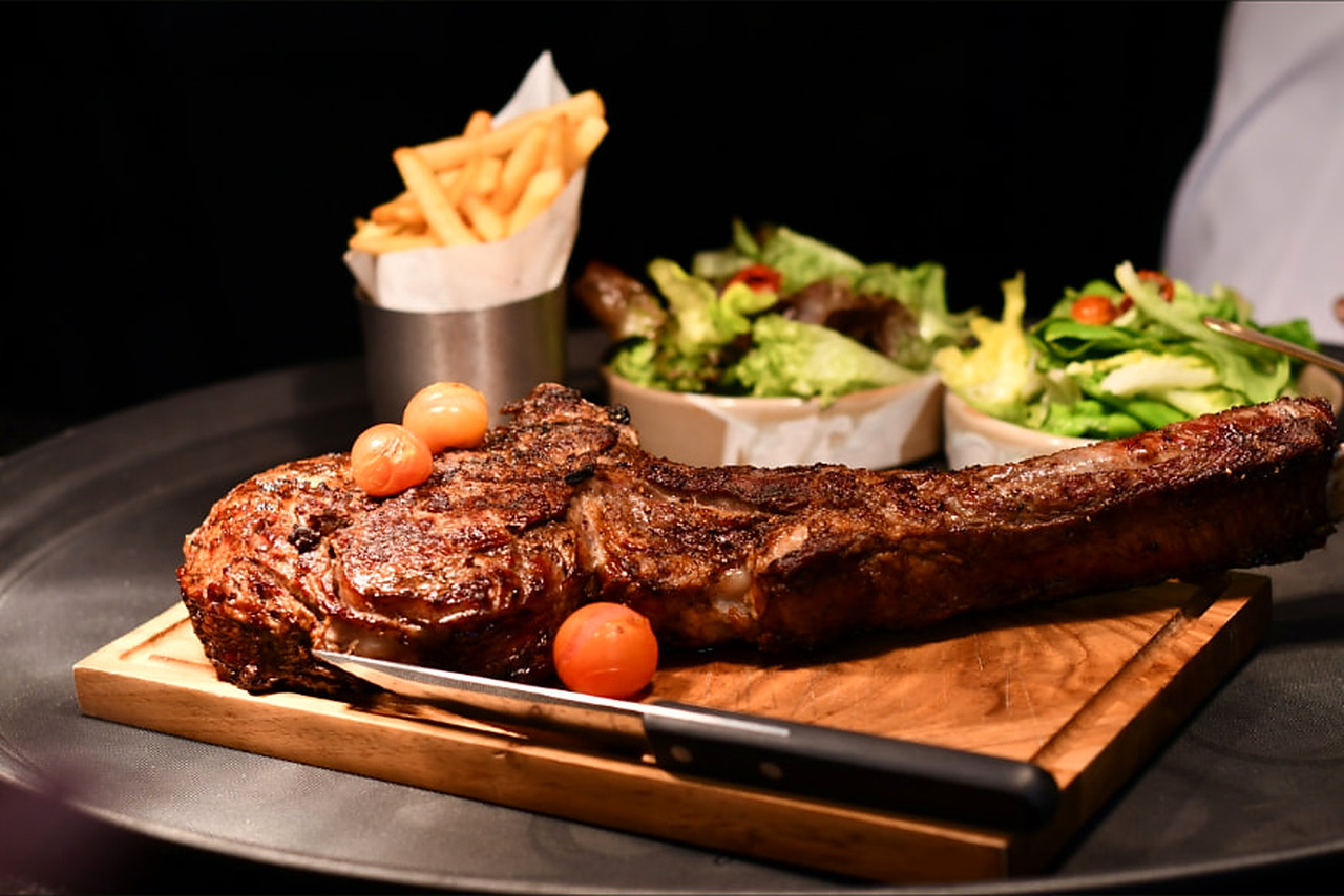 Tomahawk steak on a wooden board with fries and salads at Steak Night